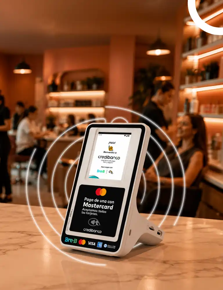 Terminal de pago Credibanco sobre el mostrador de un restaurante o cafetería, con pantalla que muestra opciones de pago con tarjeta Mastercard, rodeado de ondas luminosas que representan tecnología de pago sin contacto.