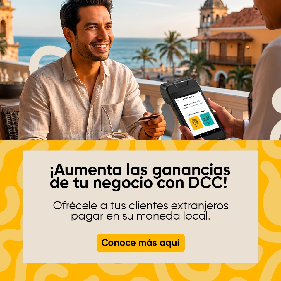 Cliente sonriente en una terraza frente al mar realiza un pago con tarjeta mientras un empleado sostiene una terminal de cobro. En la parte inferior aparece el mensaje: ‘¡Aumenta las ganancias de tu negocio con DCC! Ofrécele a tus clientes extranjeros pagar en su moneda local’ y un botón que dice ‘Conoce más aquí’.